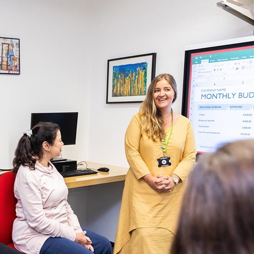A smiling Crisis support worker is leading a presentation about monthly budgeting. 